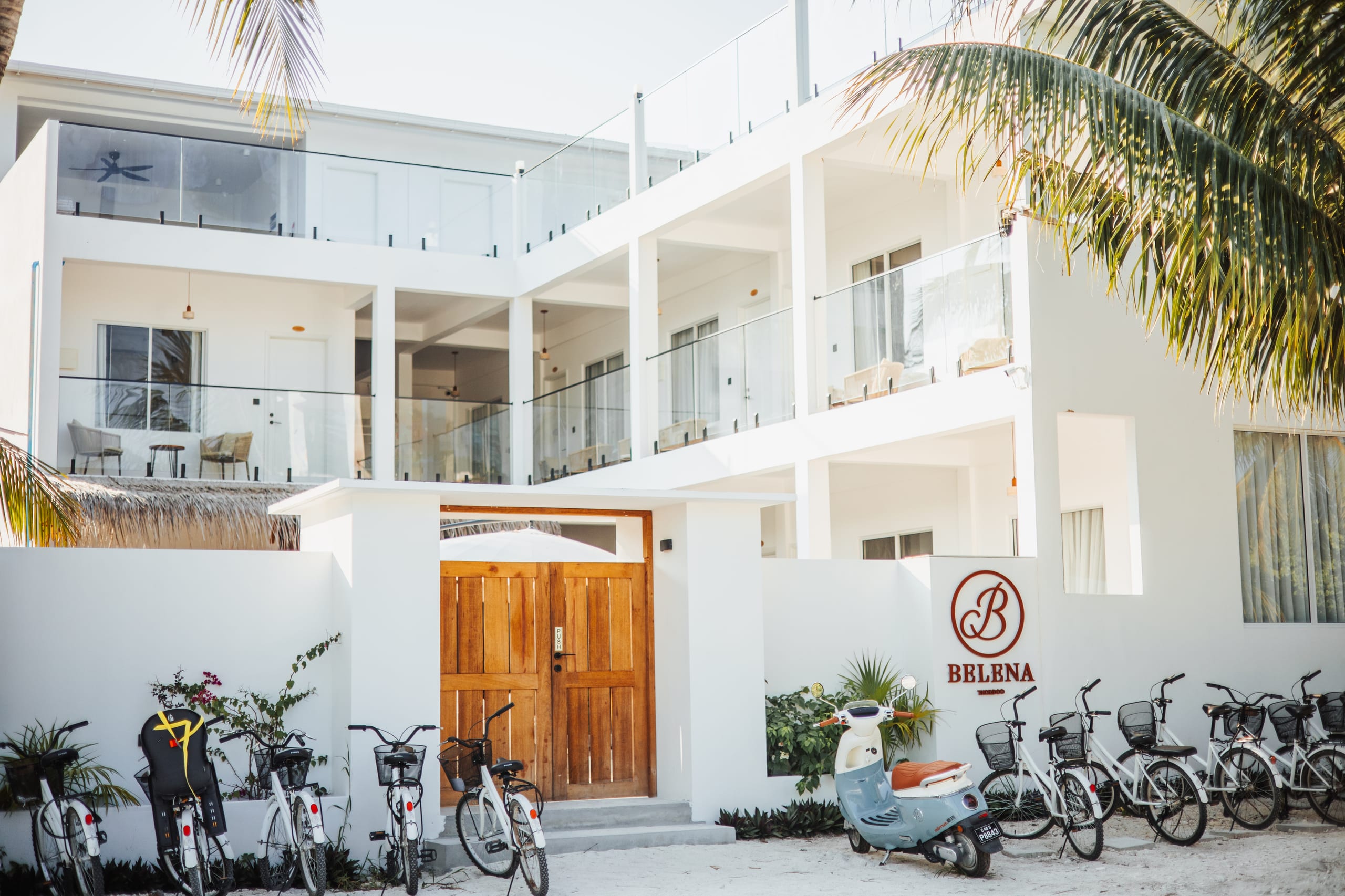 The Belena entrance beneath the palms, bicycles along the wall